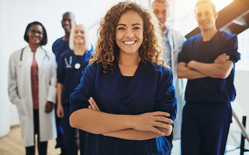 A group of nurses stands in front of a group of doctors, all smiling and dressed in medical uniforms.