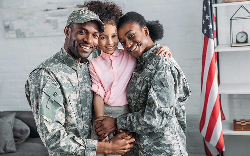 A military family smiles together in front of an American flag, showcasing their pride and unity.